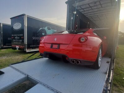 A red Ferrari California parked in the back of a truck for auto transport.