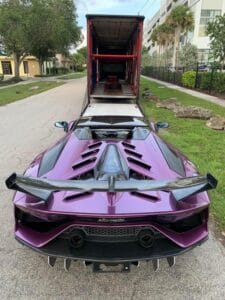 A purple Lamborghini Huracan parked in front of an auto transport truck.